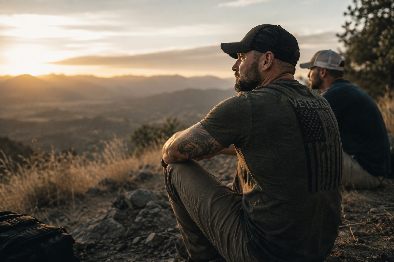 Two veterans sitting on a hillside at sunset, looking out over a quiet valley in a calm, unposed moment.